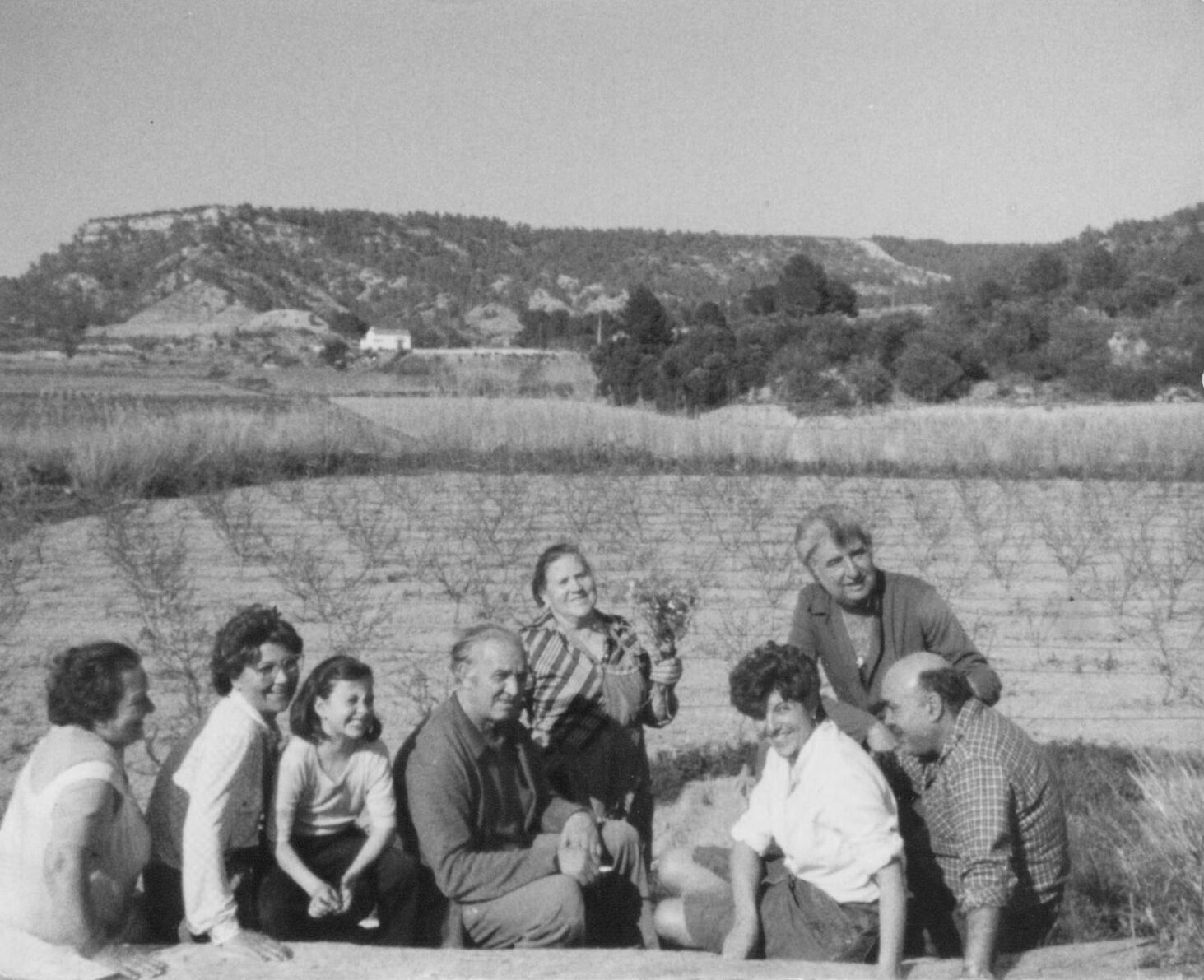 Grup de persones somrient en un camp de conreu amb muntanyes al fons, fotografia antiga