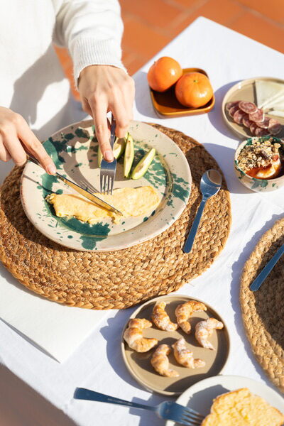 Mans tallant una truita en un plat amb l'esmorzar servit a taula