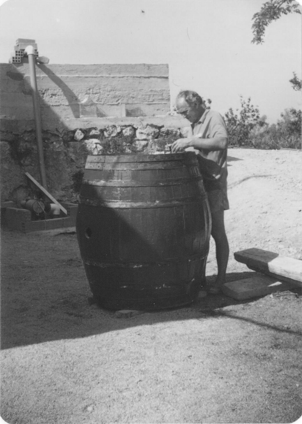 Home treballant amb una bóta de fusta al pati de la masia, foto antiga