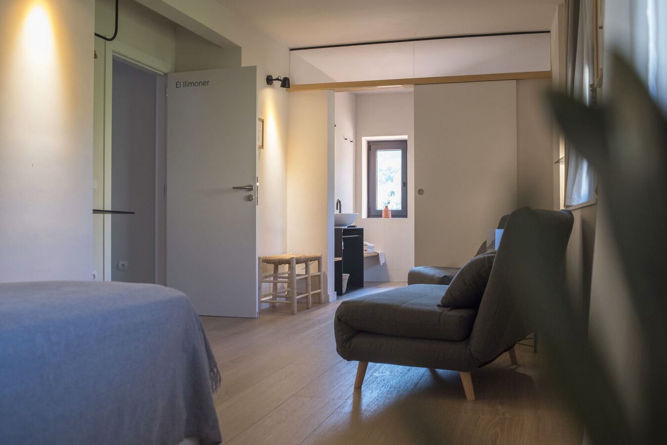 Habitació El Llimoner amb porta retolada, bany al fons i butaca gris