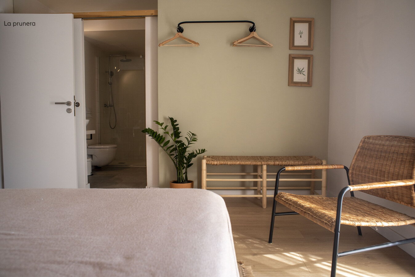 Habitació La Prunera amb penjadors, cadira de vímet i bany obert
