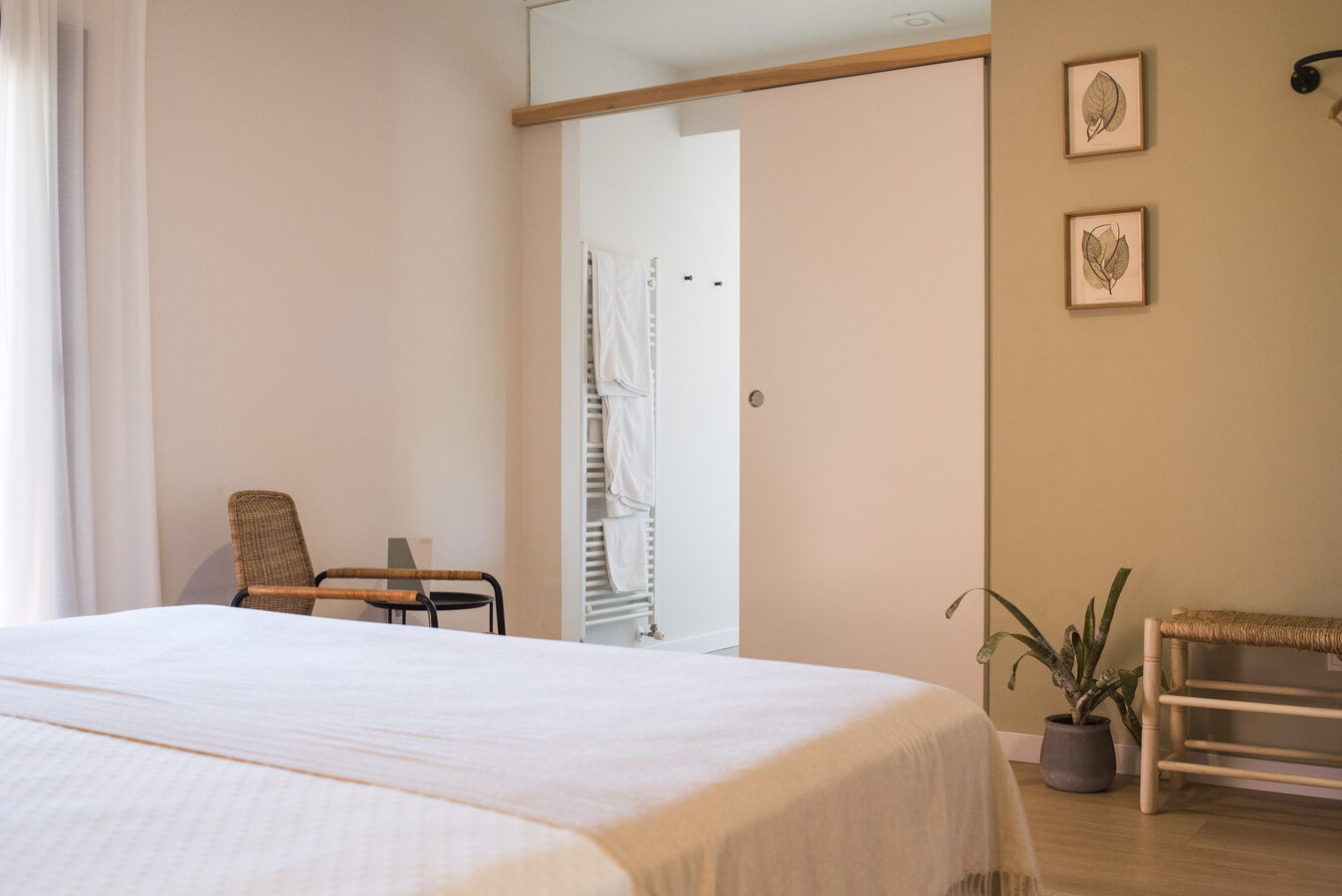 Racó d'habitació amb tovalloler blanc, cadira de vímet i planta