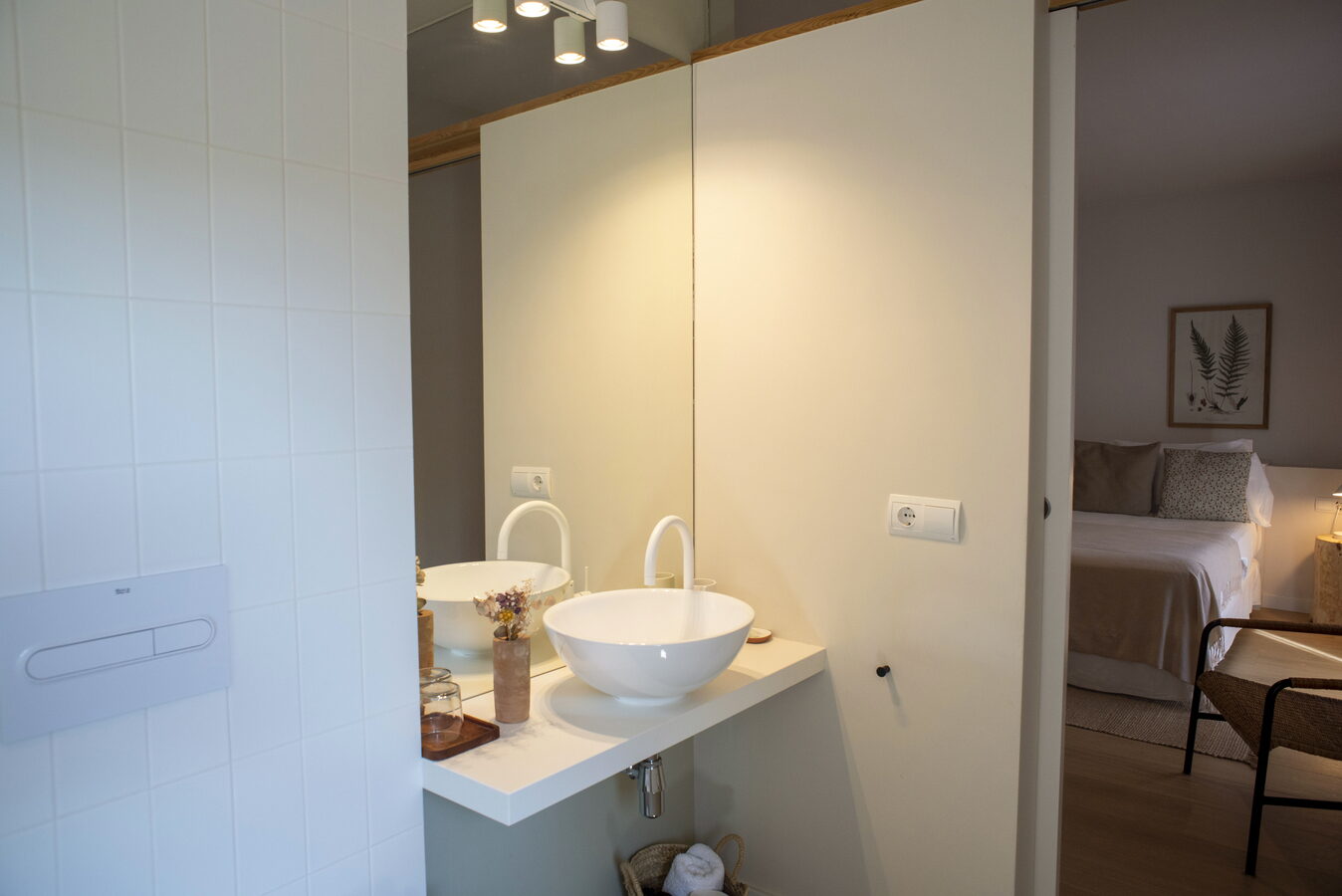 Lavabo de bany amb pica rodona blanca i habitació al fons