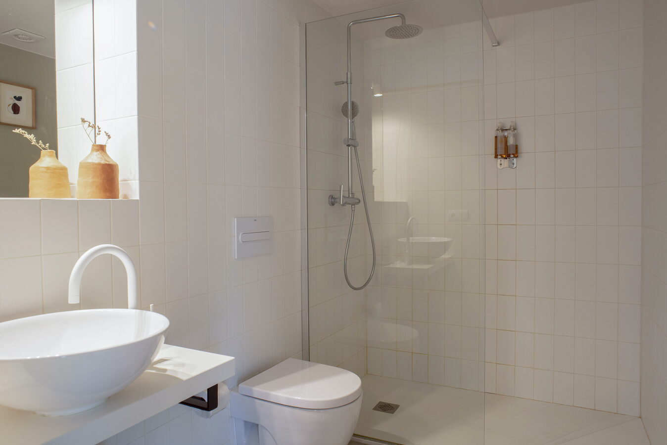 Bany amb dutxa de vidre, lavabo sobre taulell i gerros de fang