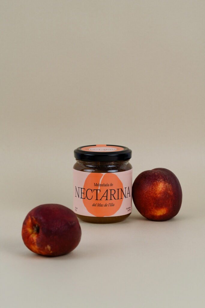 Pot de melmelada de nectarina acompanyat de dues nectarines vermelles