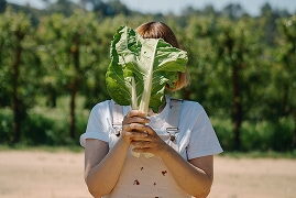 Noia tapant-se la cara amb una col davant les vinyes de la finca