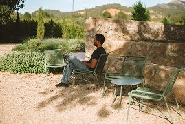Home llegint assegut en butaques al jardí amb muntanyes al fons