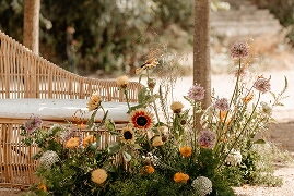 Composició de flors silvestres i gira-sols al costat d'un banc de vímet