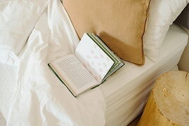 Llit blanc amb coixí de lli i llibre obert a l'habitació